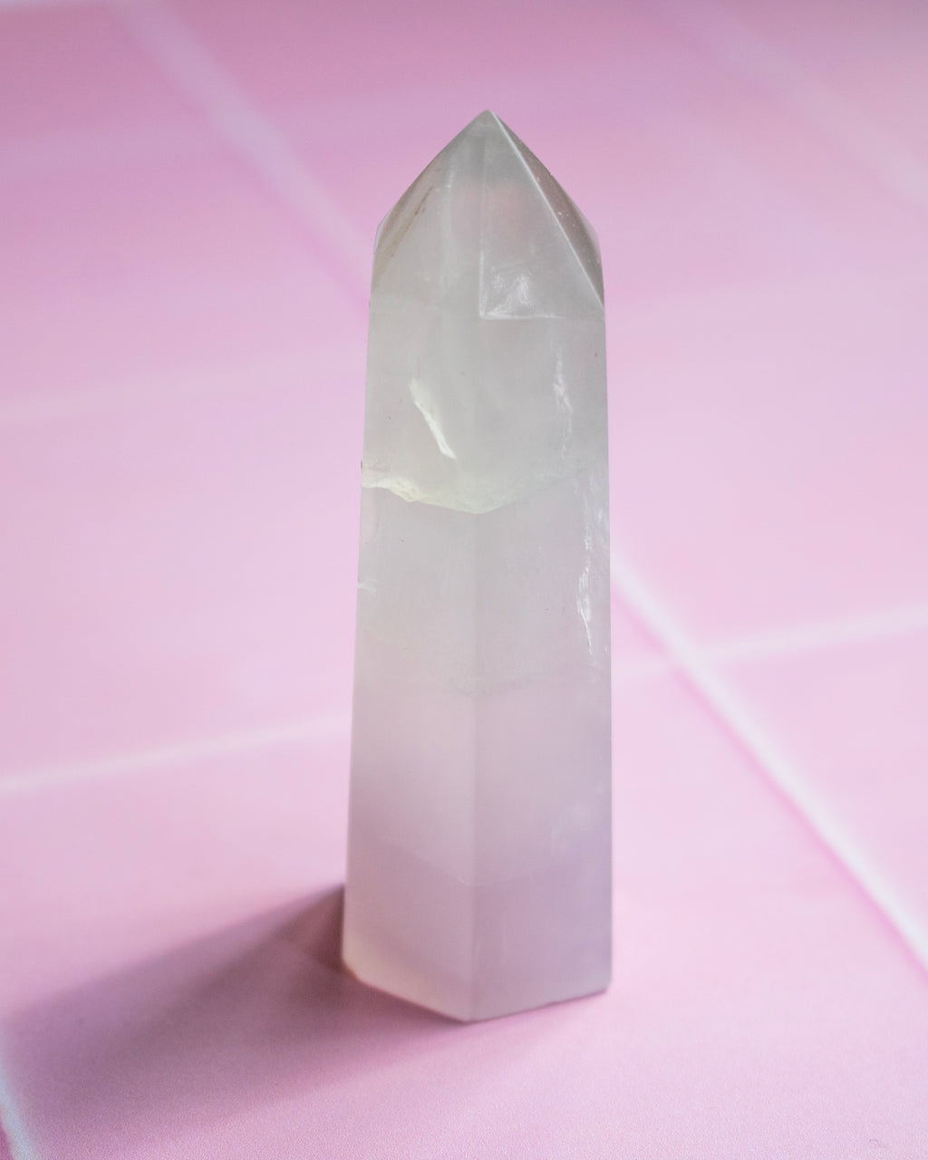 A pale pink and white crystal point tower standing upright on a pink surface with a matching pink background.