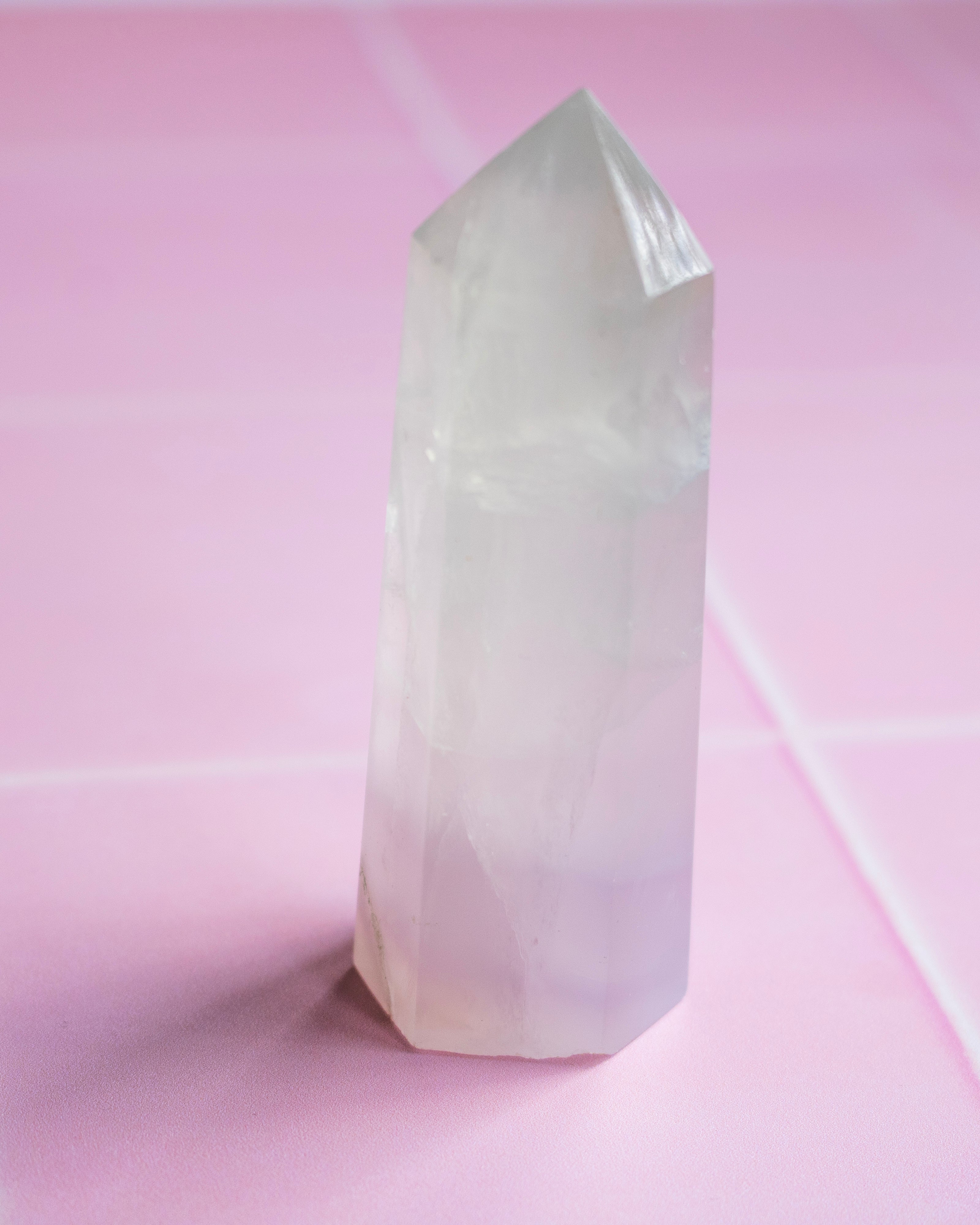 A natural pointed crystal tower, standing upright on a pink surface with a matching pink background.