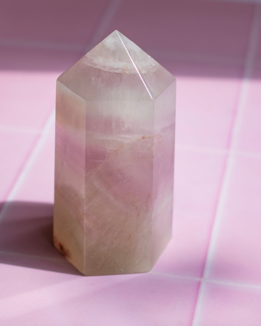 A natural crystal point tower with layered pink and white bands, standing on a pink tiled surface.