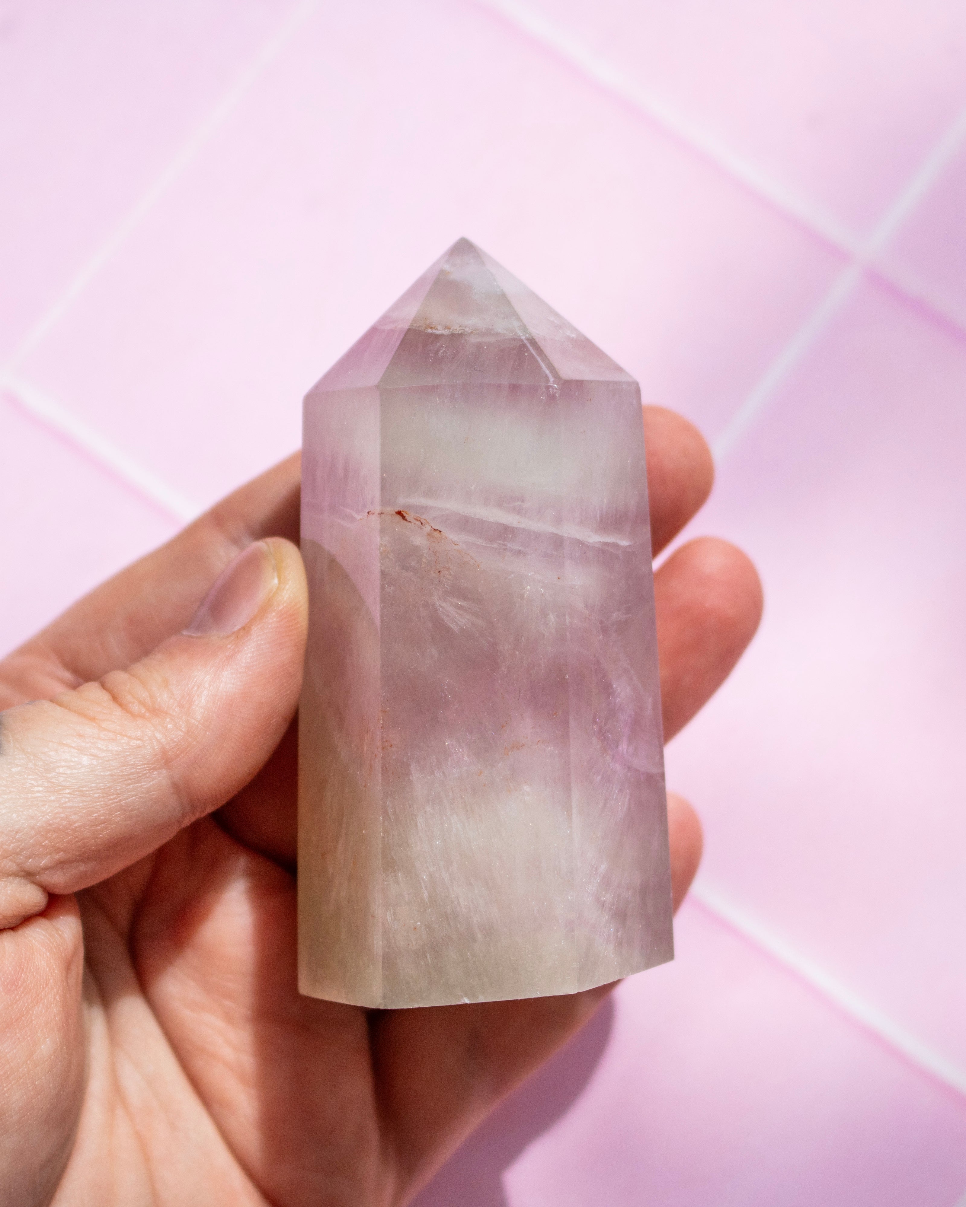 A hand holding a pointed pink crystal tower against a soft pink background.