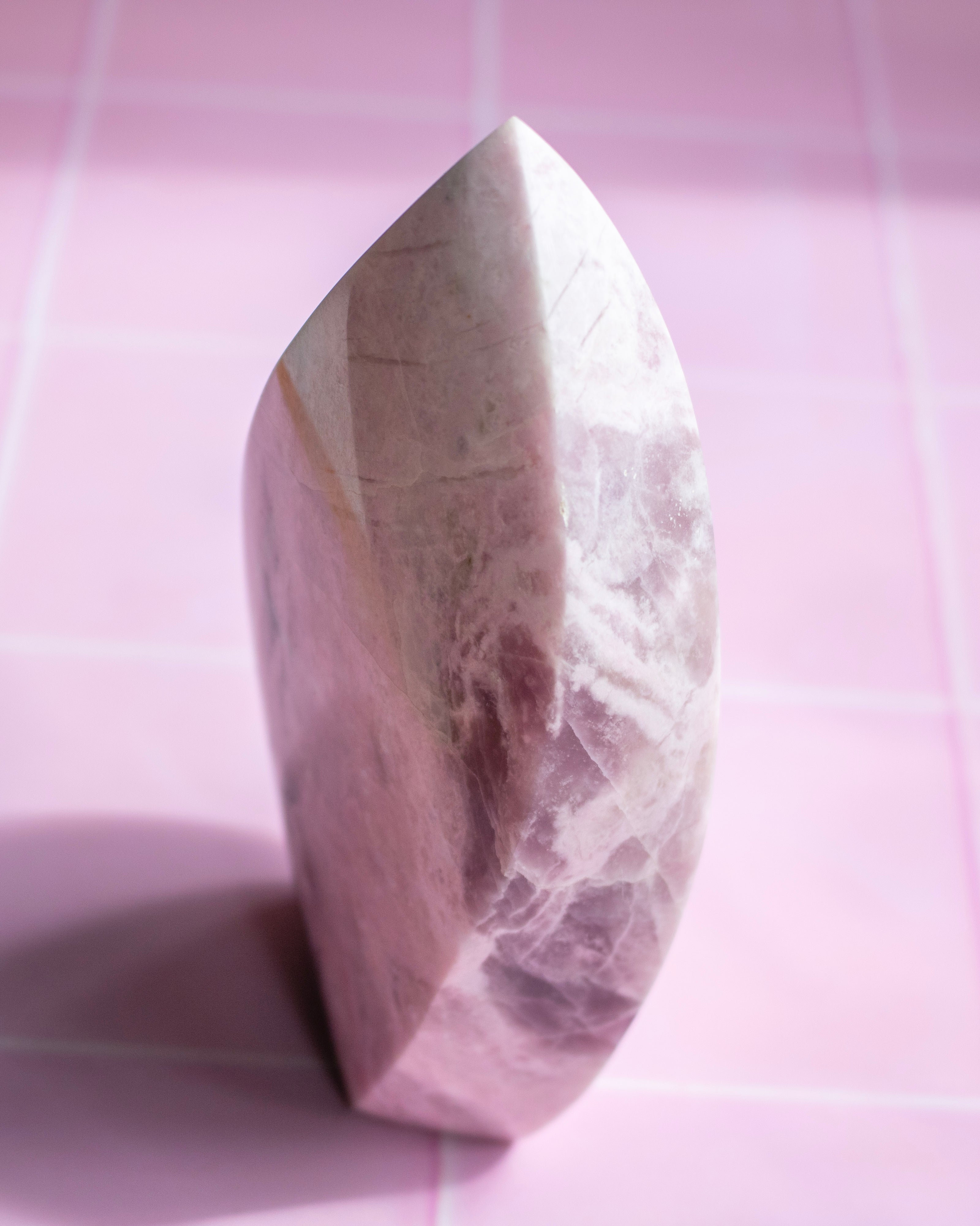 A polished pink quartz crystal point sculpture standing upright on a pink grid background.