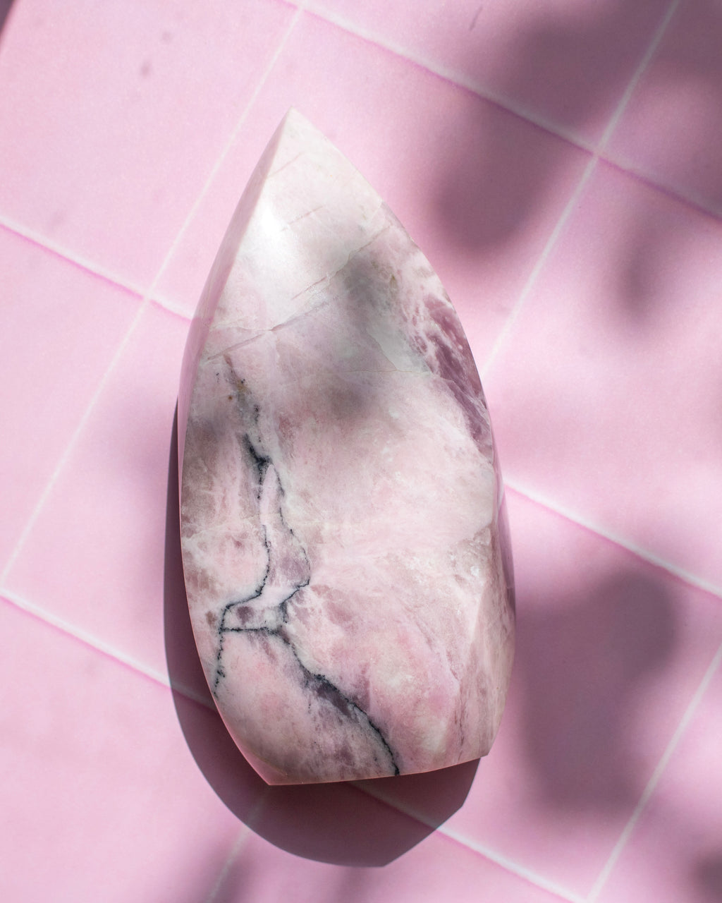 A polished pink stone with natural gray and white veining, photographed from above on a pink tiled surface with soft shadows.
