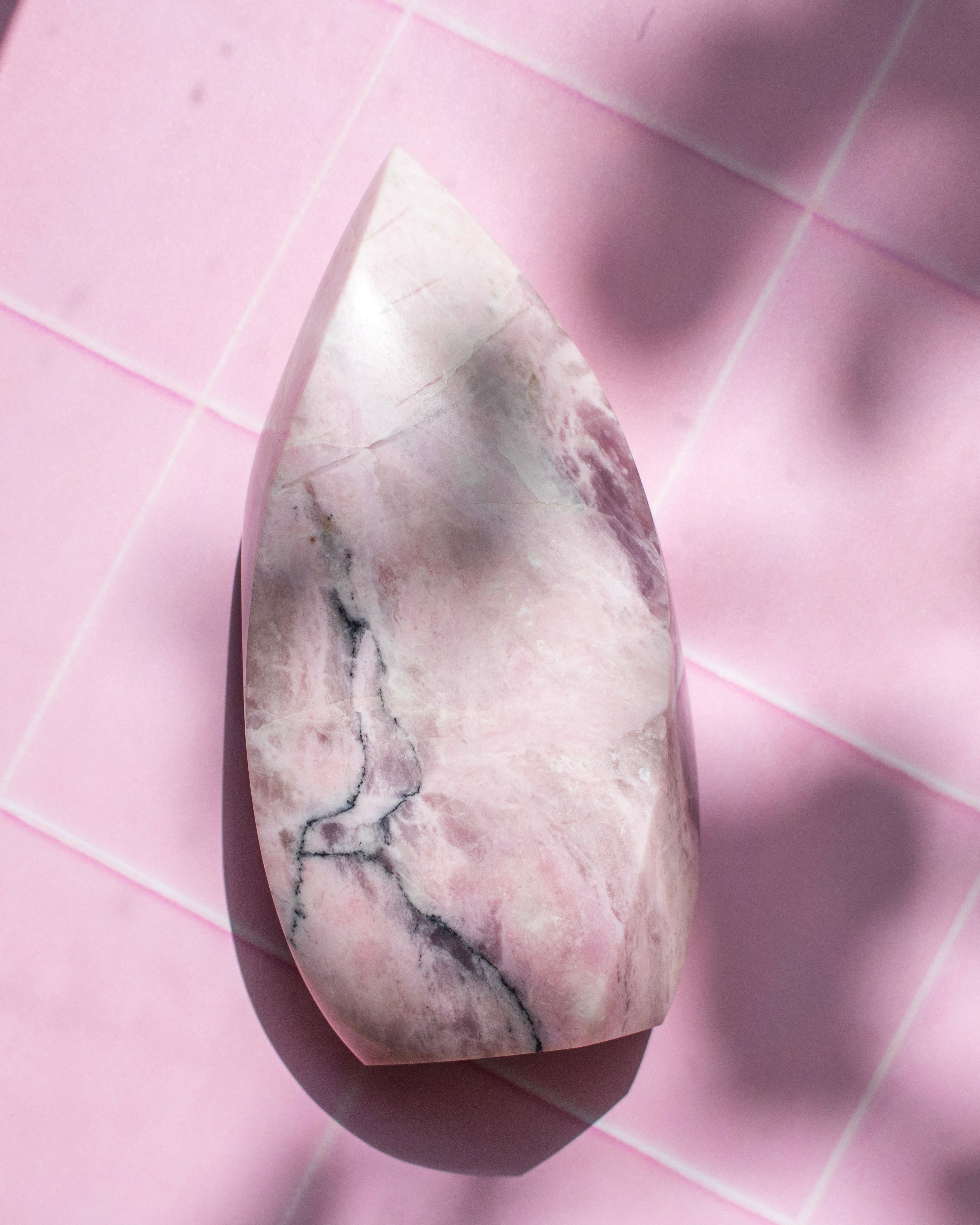 A polished pink stone with natural gray and white veining, photographed from above on a pink tiled surface with soft shadows.