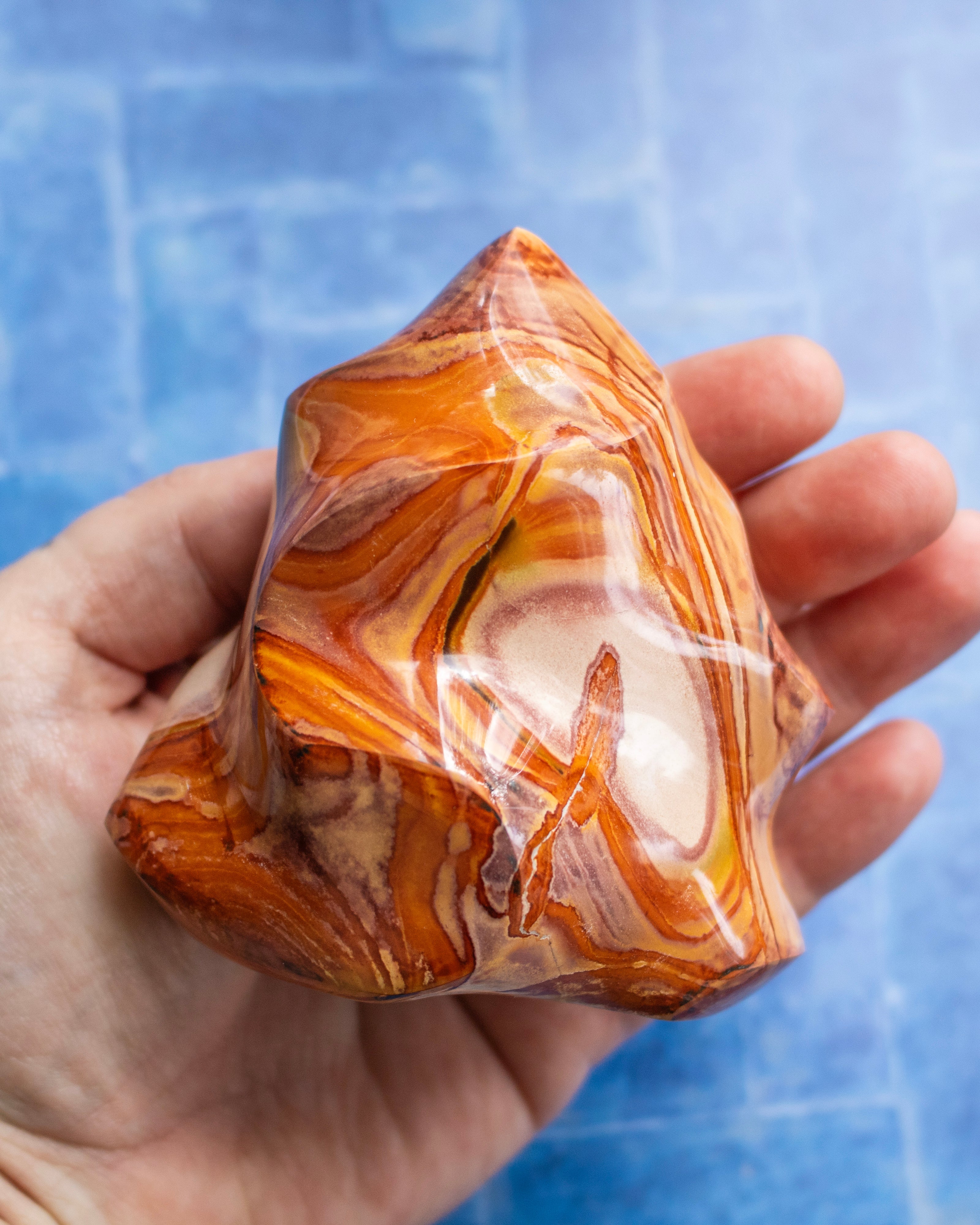 A hand holding a polished orange and yellow marbled stone against a blue tiled background.