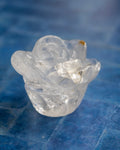 A small translucent clear crystal rose figurine with a textured, layered petal design, resting on a blue textured surface.