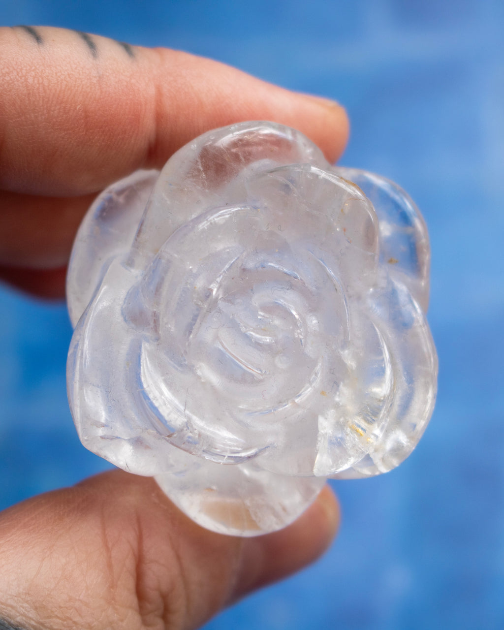 A hand holding a carved clear rose-shaped object against a bright blue blurred background.