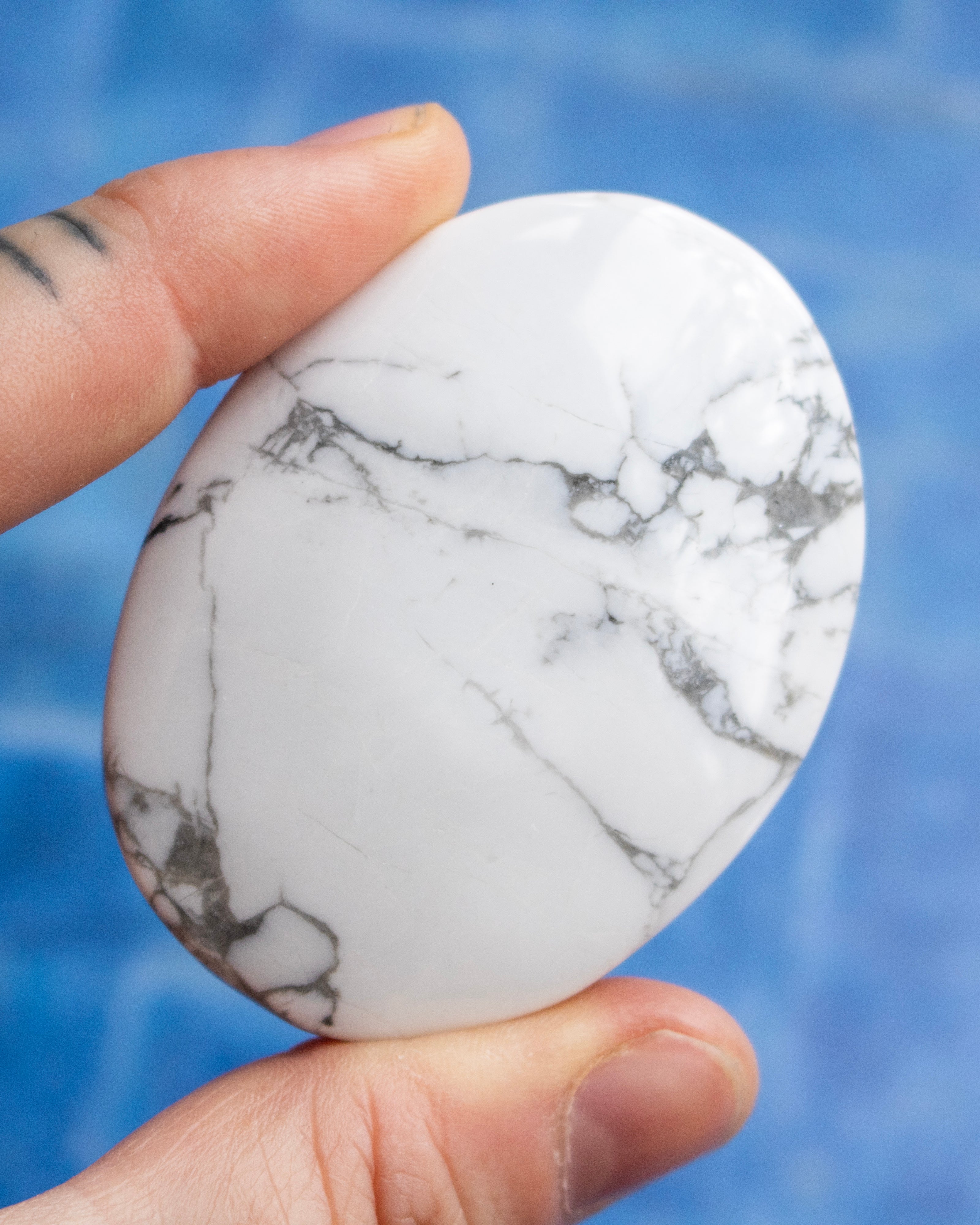 A hand holding a polished white marble stone with gray veining, set against a bright blue background.