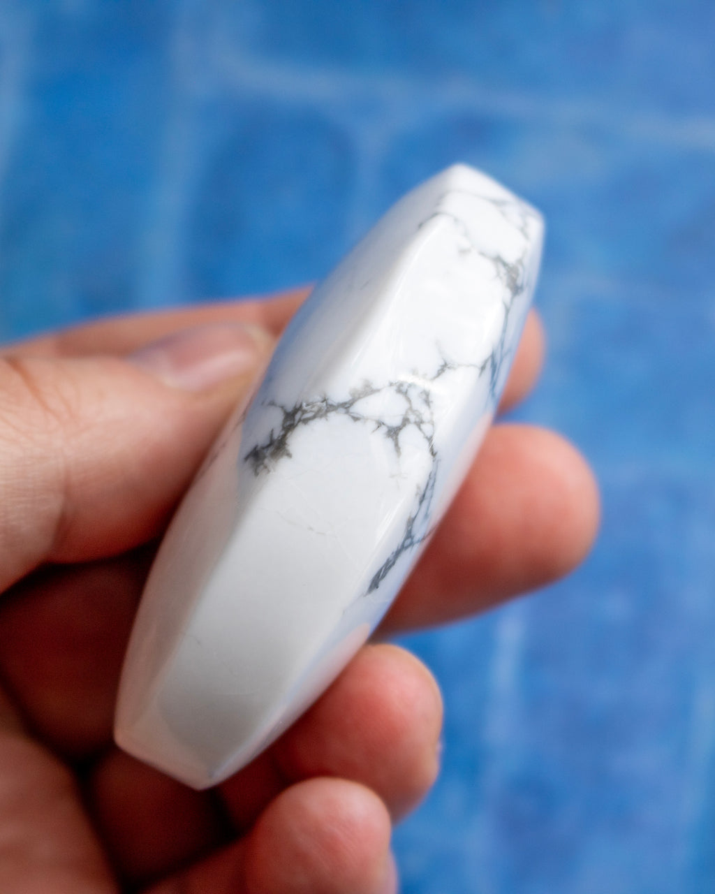 A hand holding a polished white stone with gray veining, set against a blurred blue background.