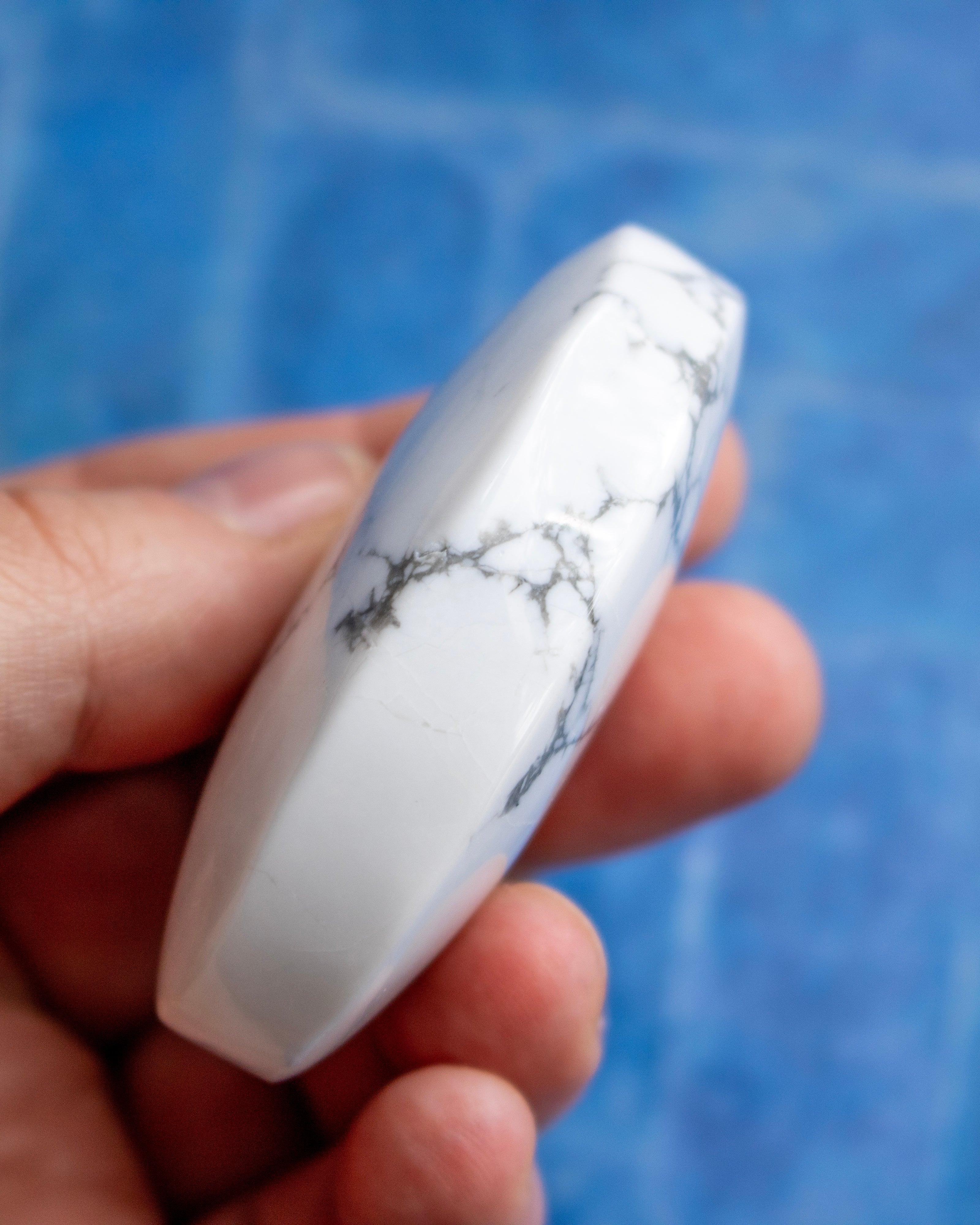 A hand holding a polished white stone with gray veining, set against a blurred blue background.