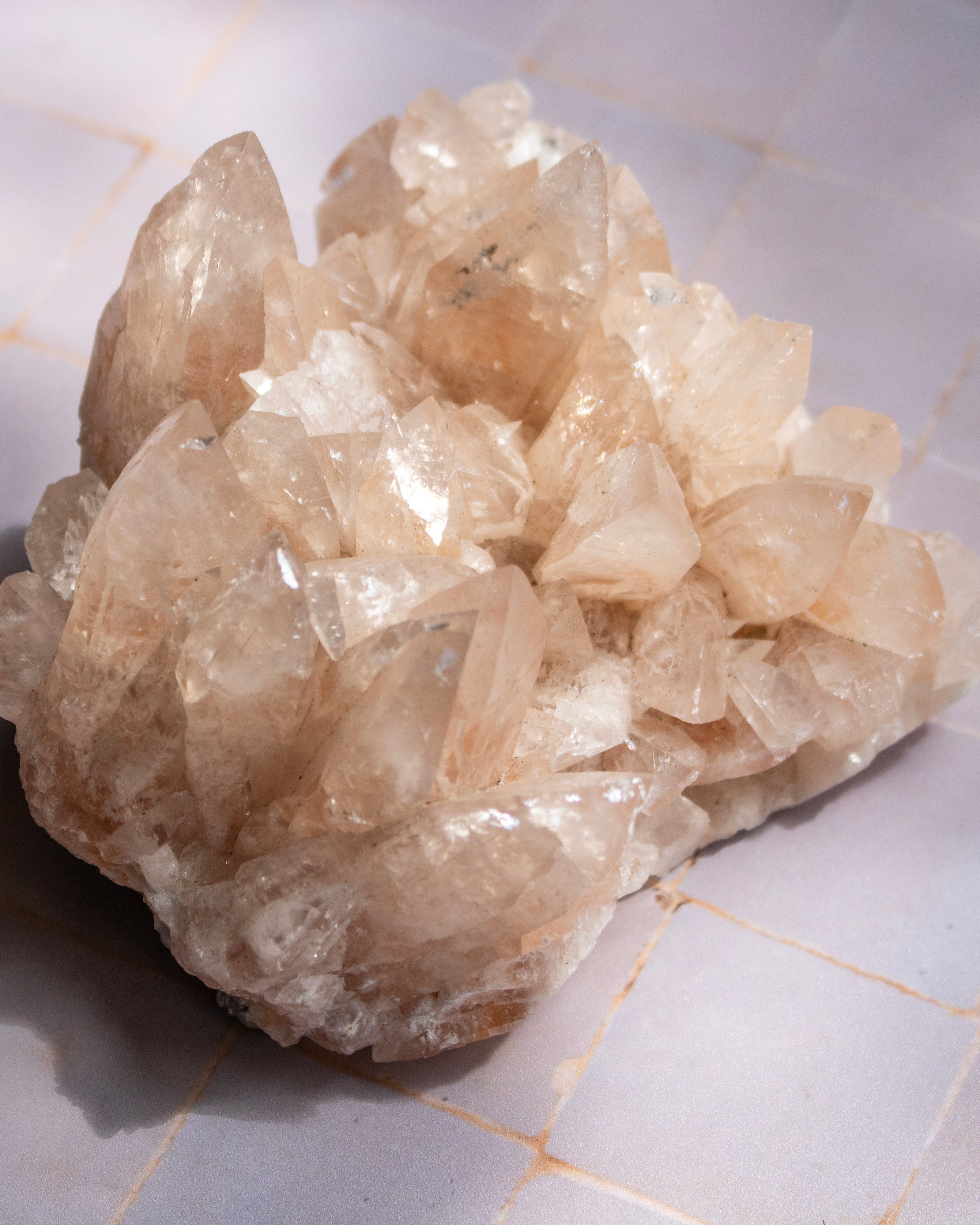 A natural crystal cluster with pale peach and translucent white tones, resting on a light-colored tiled surface.
