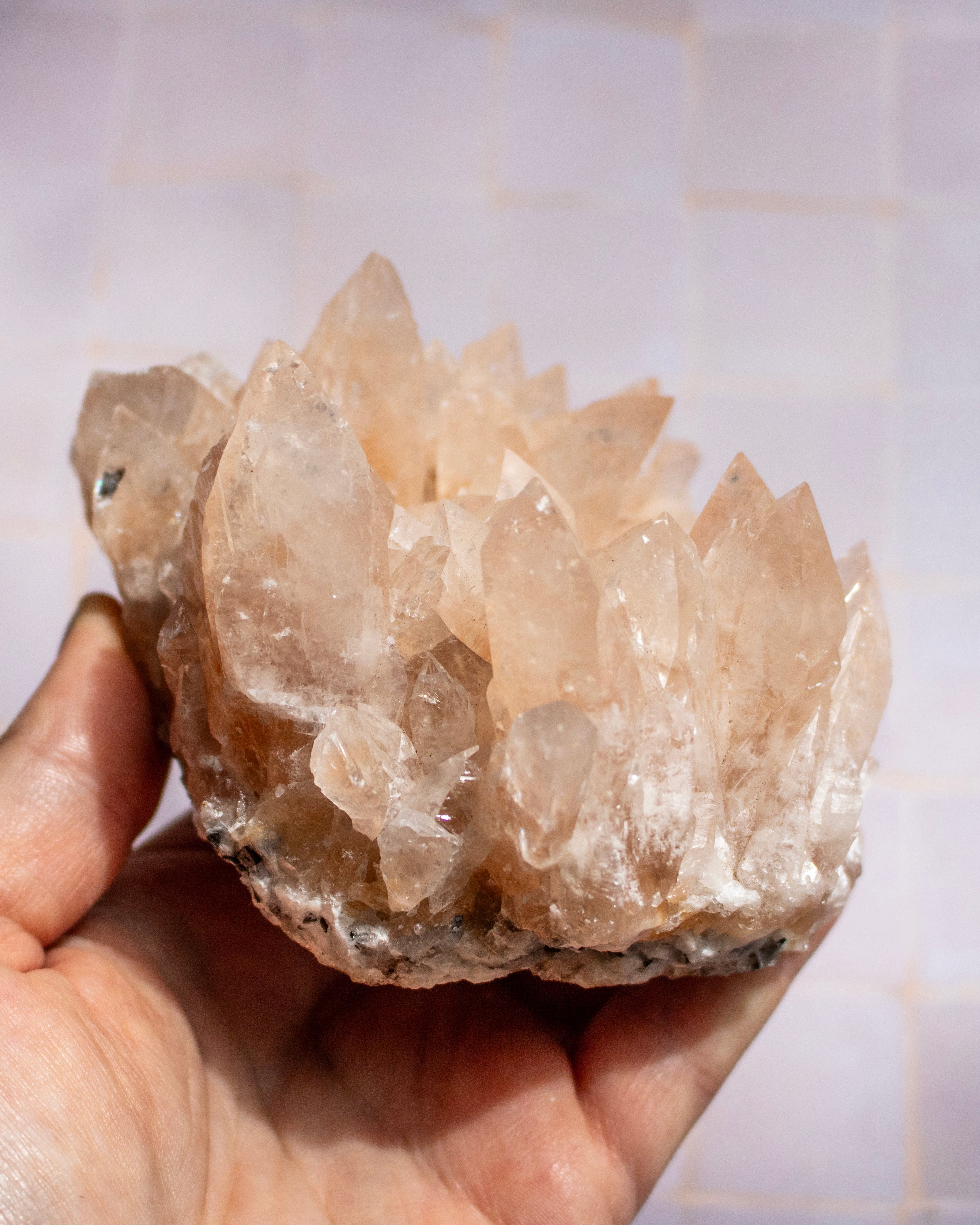 A hand holding a raw crystal cluster geode against a light tiled background.