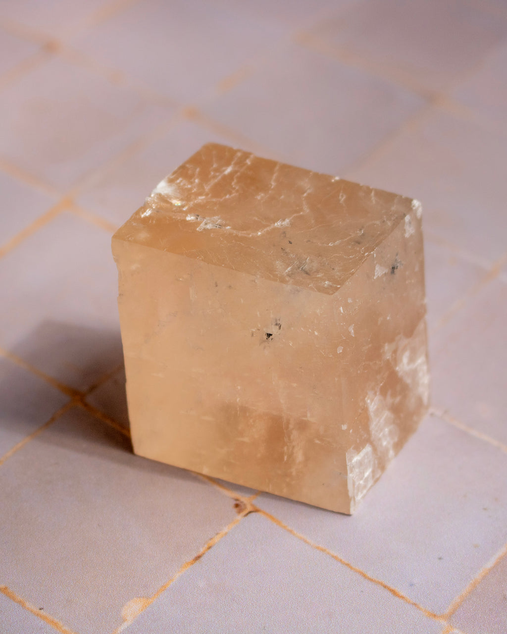 A raw, rough-cut cube of translucent pale peach quartz on a light beige tiled surface.