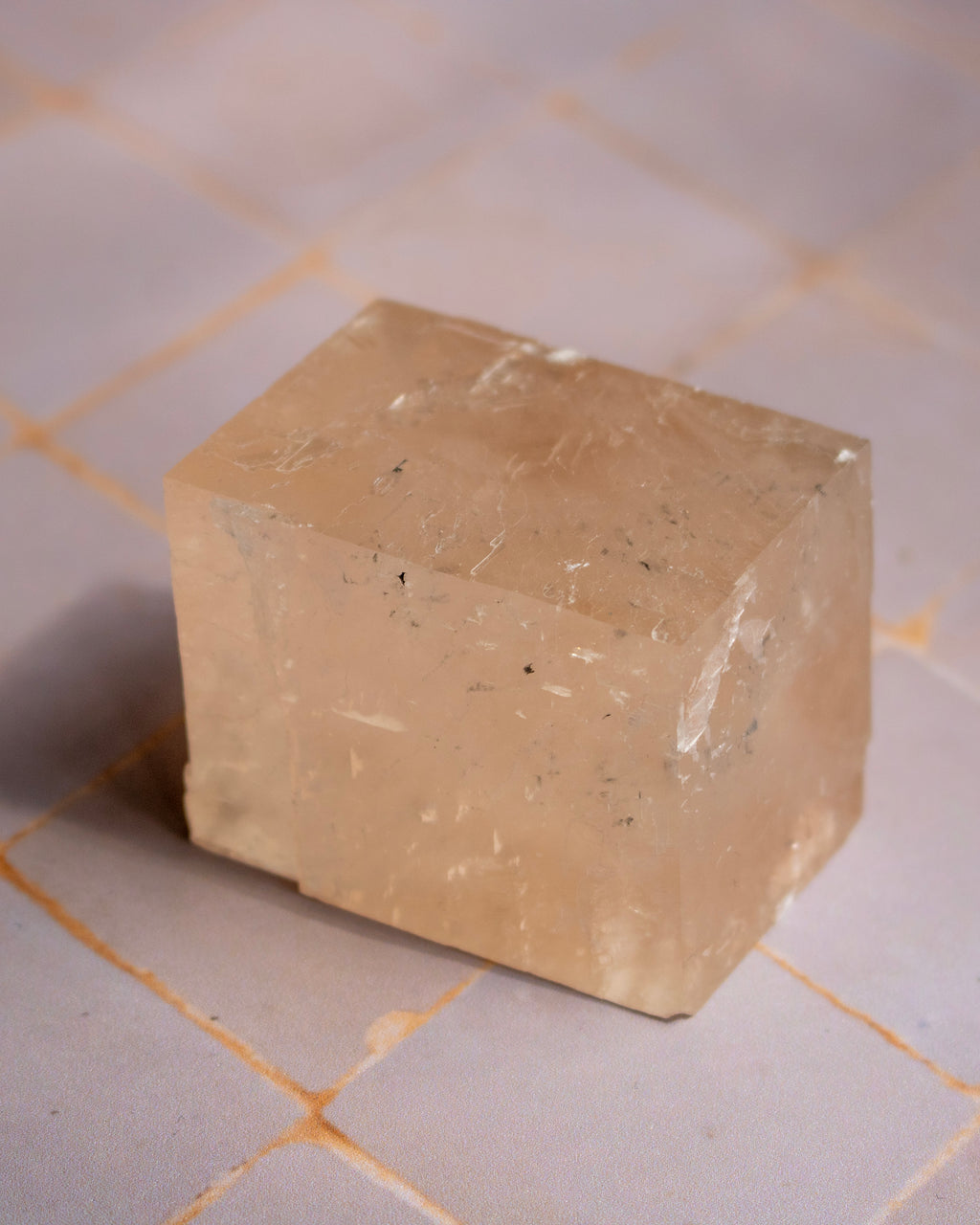 A translucent pale peach-beige rectangular stone or crystal block with natural inclusions, photographed on a light tiled surface.