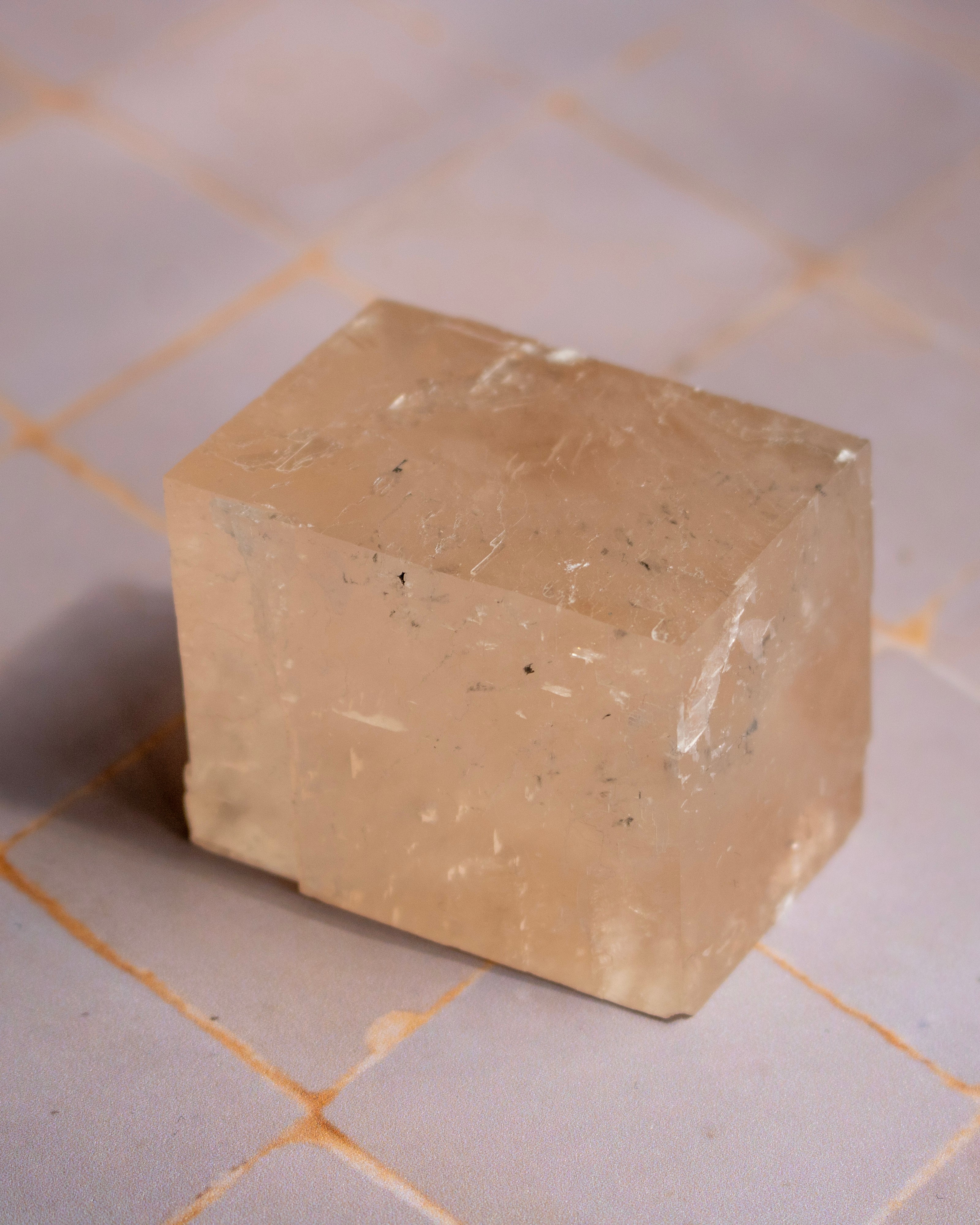 A translucent pale peach-beige rectangular stone or crystal block with natural inclusions, photographed on a light tiled surface.