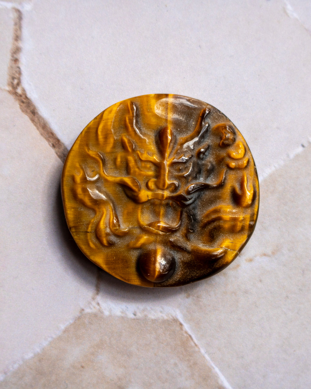 A round, carved amber-brown stone pendant or button featuring a raised dragon motif, displayed on a light beige stone surface.