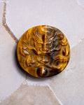 A round, carved amber-brown stone pendant or button featuring a raised dragon motif, displayed on a light beige stone surface.