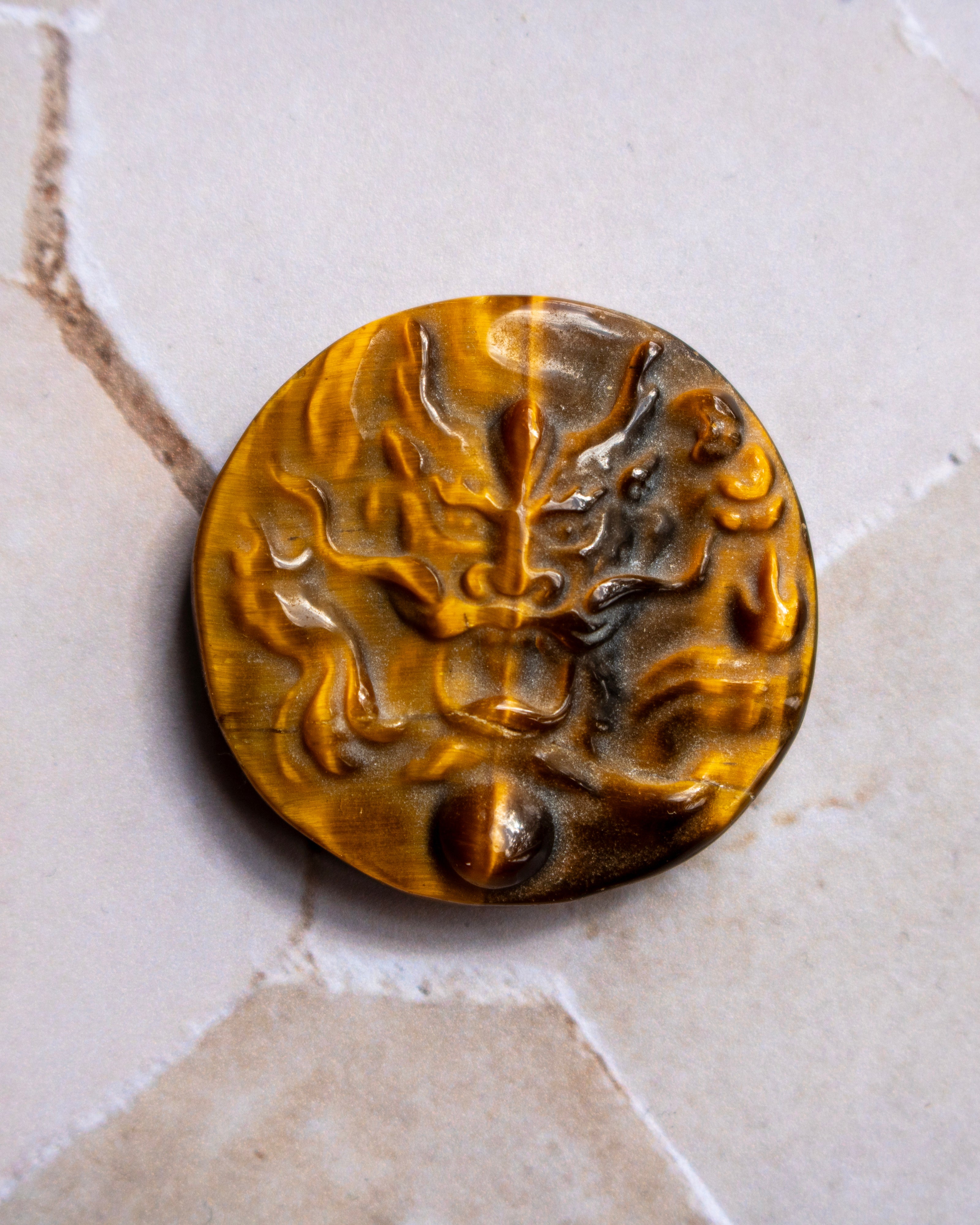 A round, carved amber-brown stone pendant or button featuring a raised dragon motif, displayed on a light beige stone surface.
