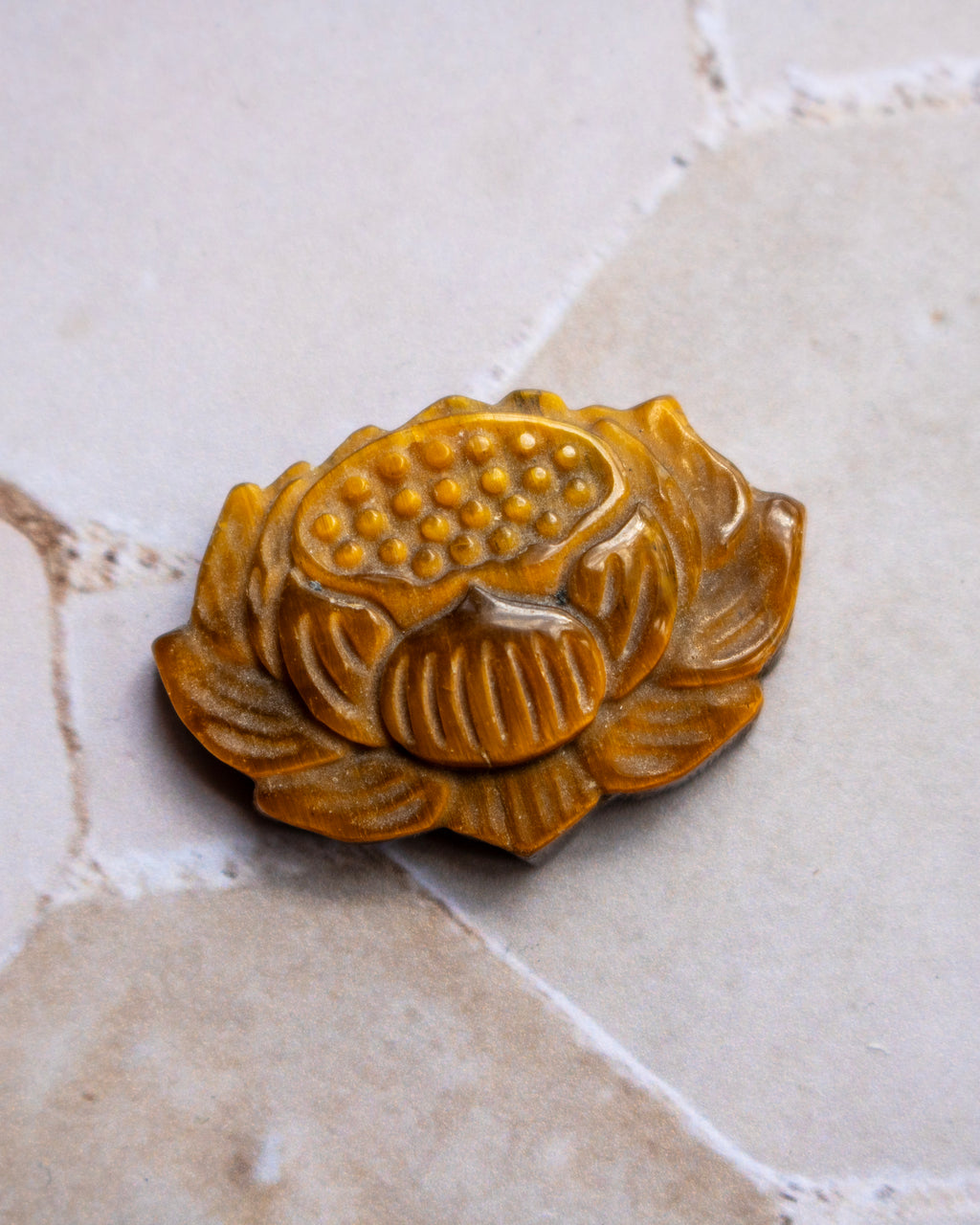 A carved brown lotus flower pendant or ornament with detailed ridges and a dotted center, resting on a light beige stone surface.